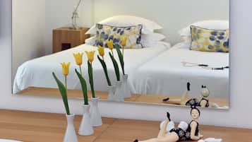 A bedroom with a bed, a nightstand, a mirror, and vases with flowers.