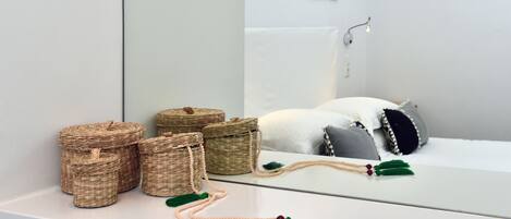 Casa de banho com lavatório branco, cestos de vime, espelho e porta-toalhas.