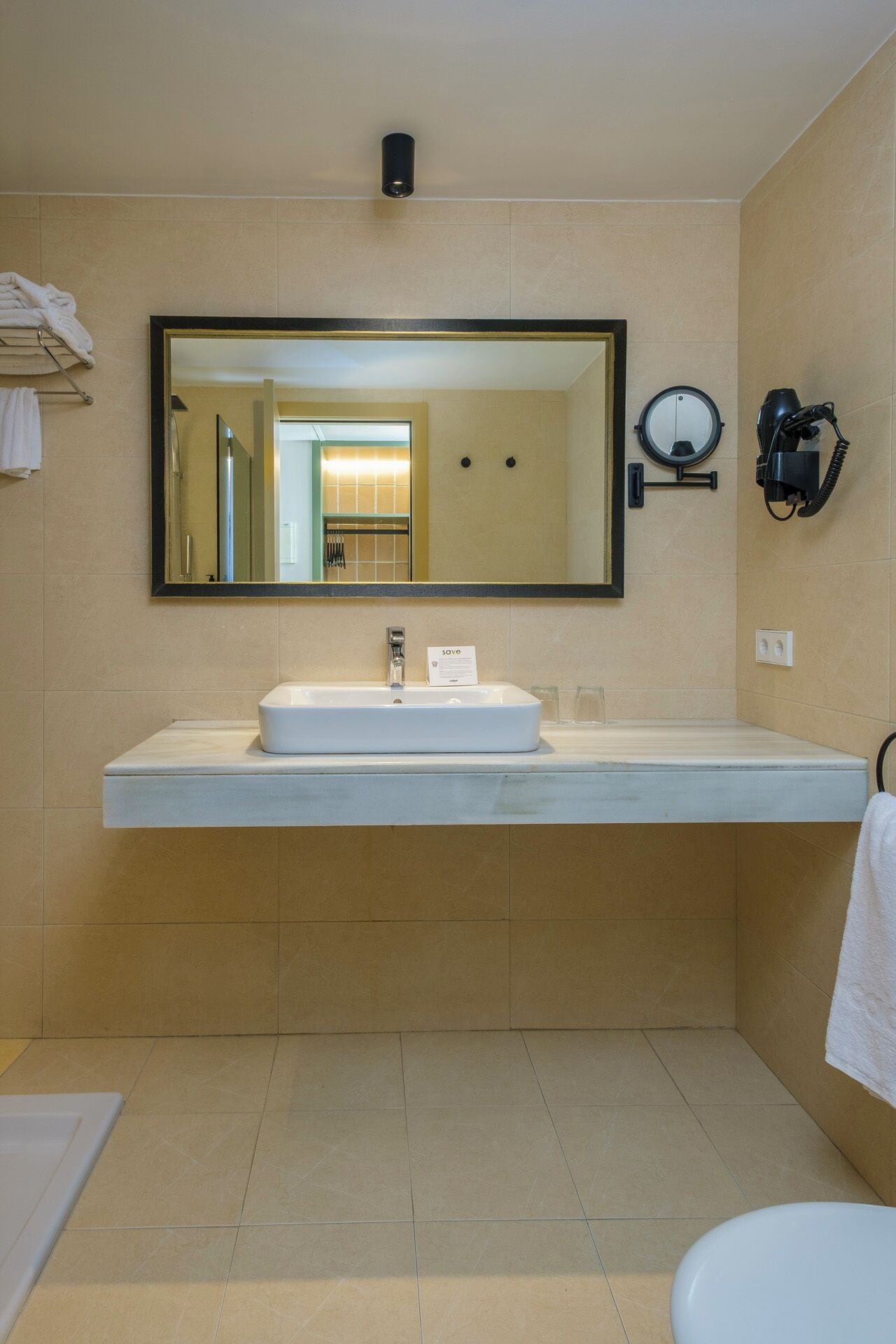 A bathroom with a large mirror, a sink, a towel rack, and a hairdryer.