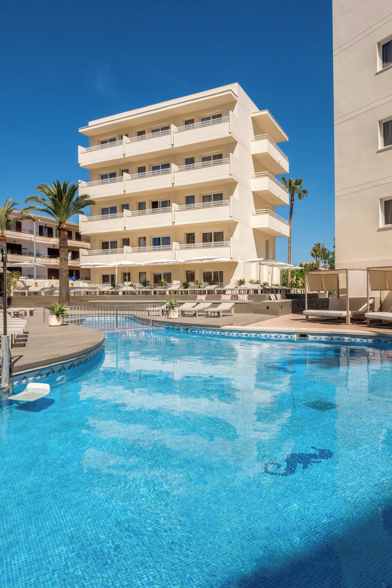 Un hotel con piscina, varios balcones y palmeras.
