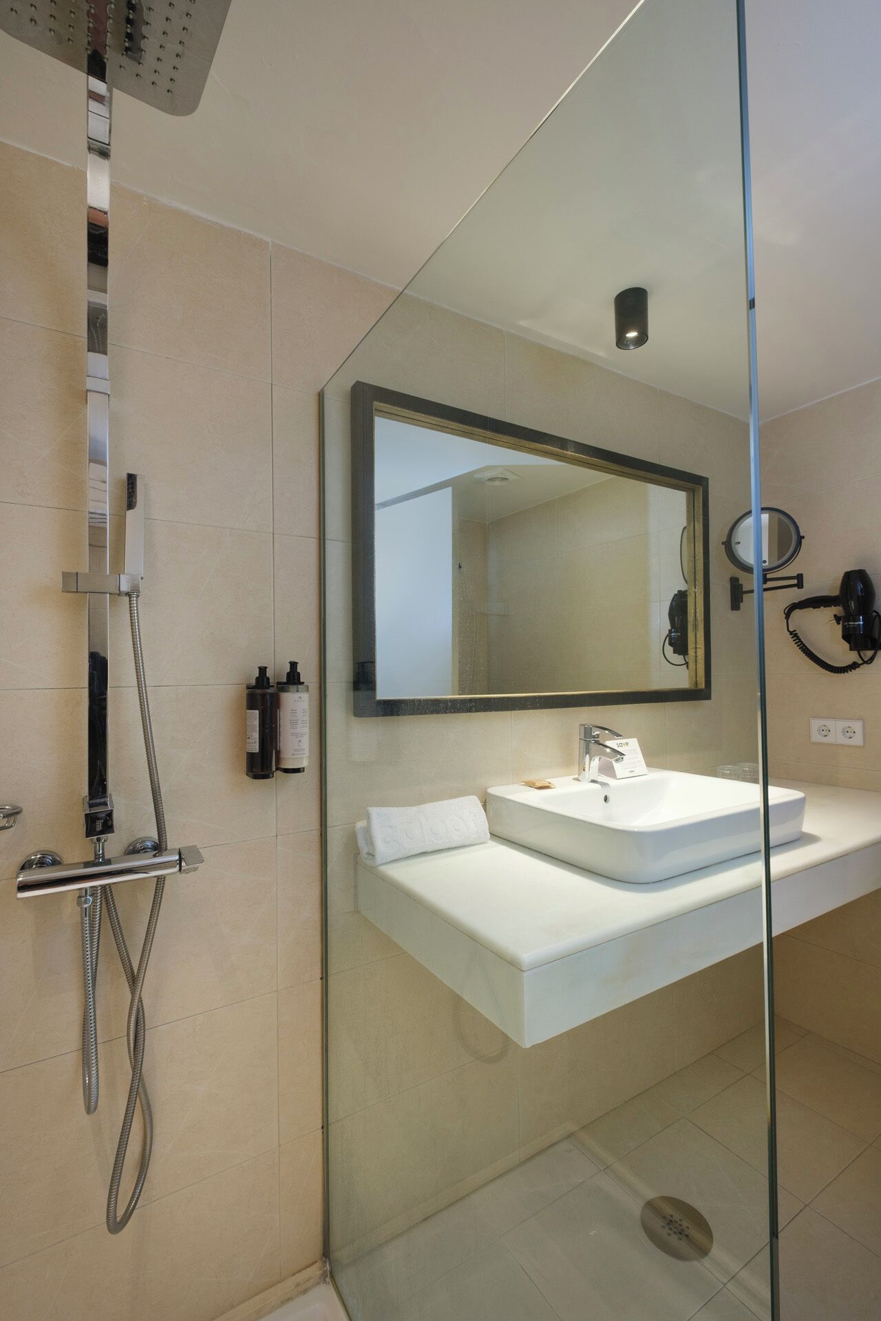 Un baño moderno con cabina de ducha de vidrio, un lavabo blanco y un espejo grande.