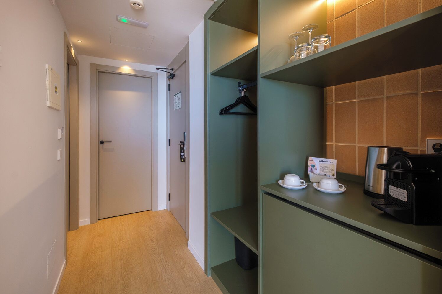 A hotel corridor with a door, a coat rack, and a coffee station with cups and a coffee maker.