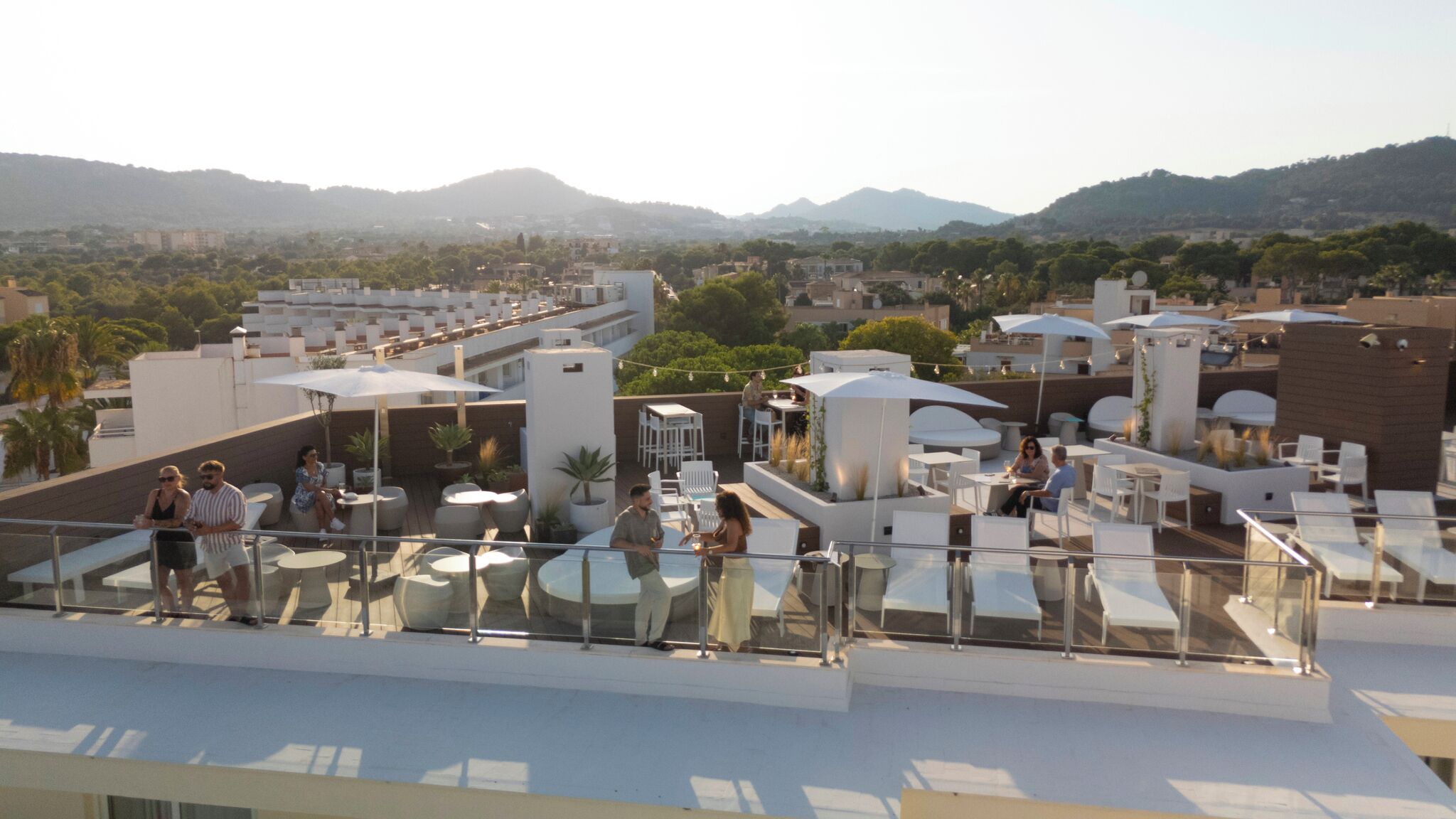 Une terrasse sur le toit, dotée d’un espace extérieur avec des sièges et des tables, entourée d’immeubles et offrant une vue sur un paysage montagneux.