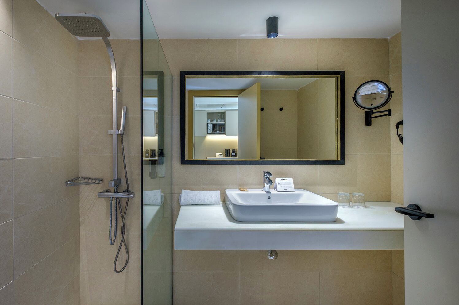 Un baño moderno con cabina de ducha de vidrio, un espejo grande, un lavabo y un reloj en la pared.