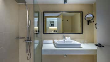 Un baño moderno con cabina de ducha de vidrio, un espejo grande, un lavabo y un reloj en la pared.