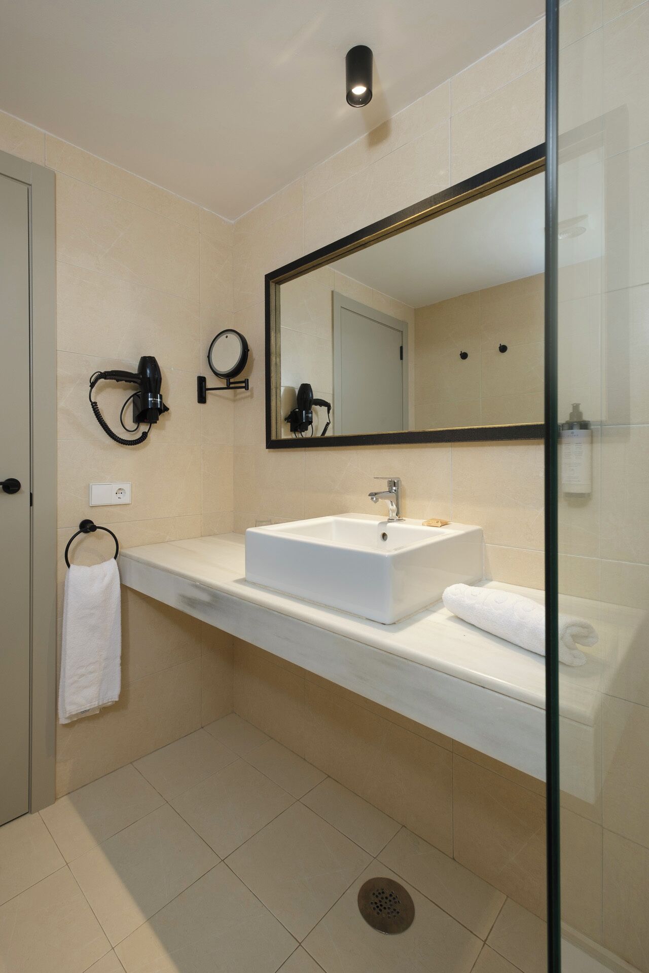 A modern bathroom with a white sink, a large mirror, and a hairdryer on the wall.
