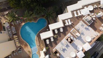 Vista aérea de um hotel com piscina em formato de coração, áreas de estar ao ar livre e um bar no terraço.