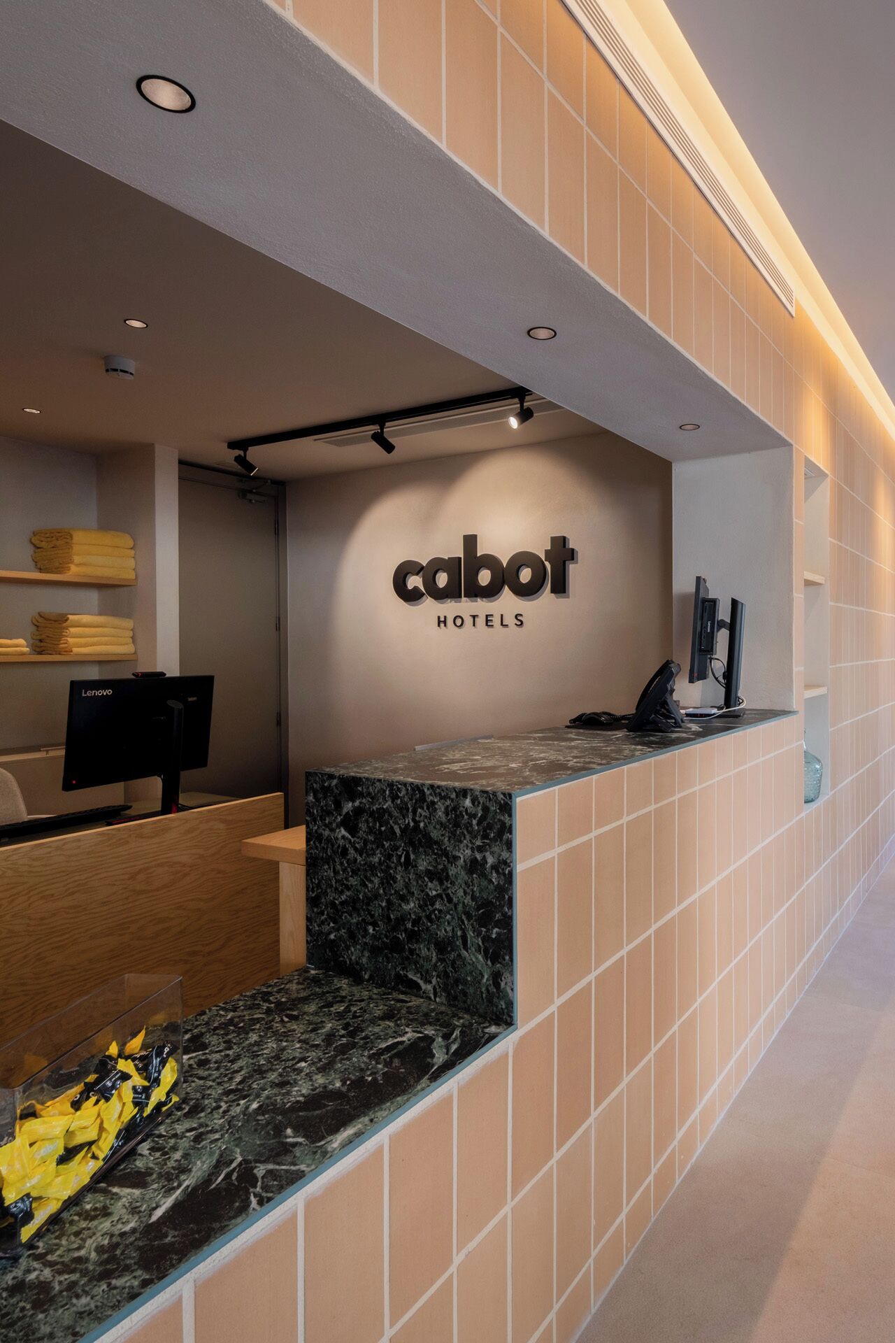 Un comptoir d’accueil d’hôtel avec une enseigne « Cabot Hotels », un ordinateur et un comptoir dont la surface ressemble à du marbre.