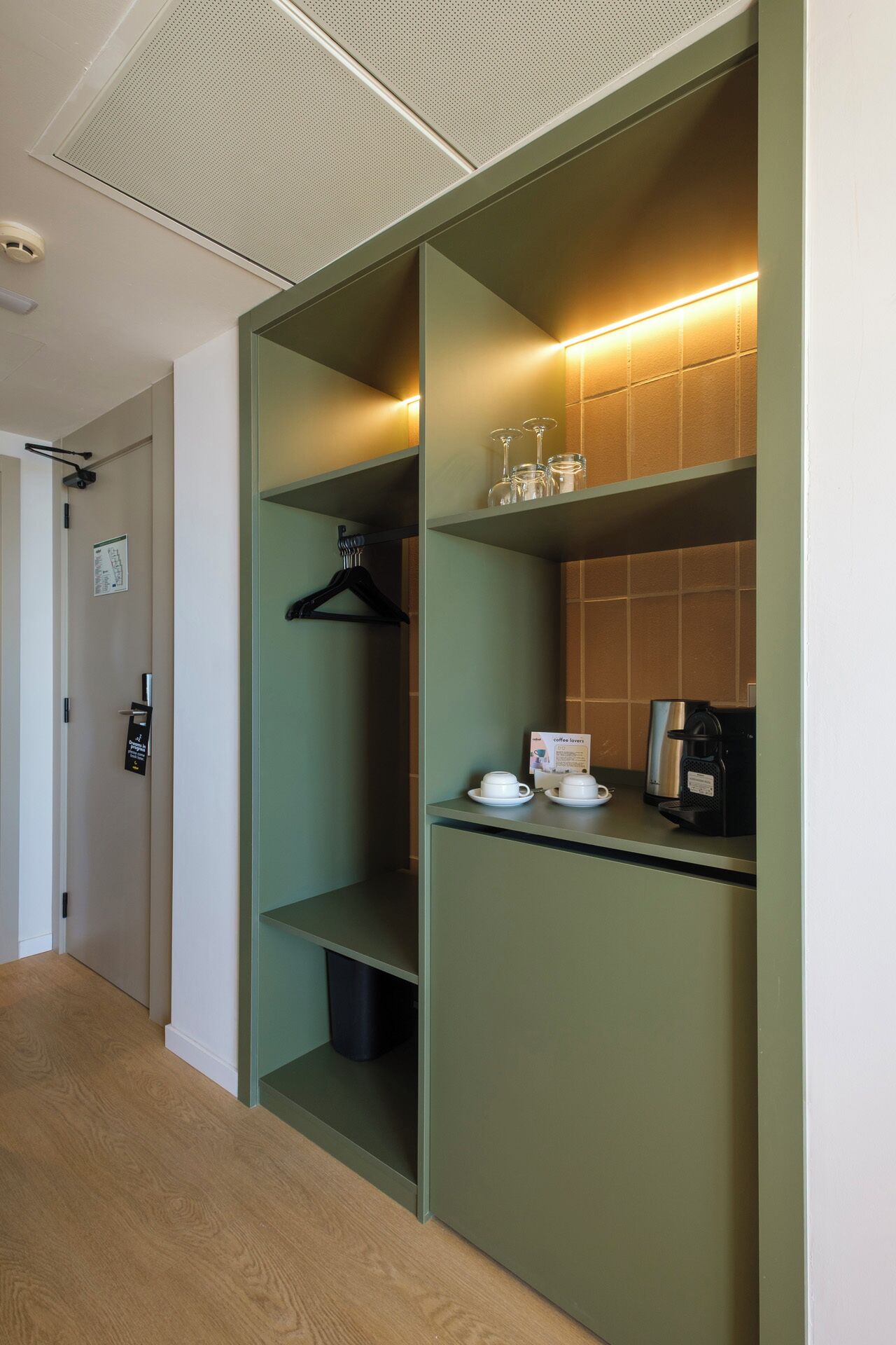 Una habitación de hotel con kitchenette, perchero y cafetera.