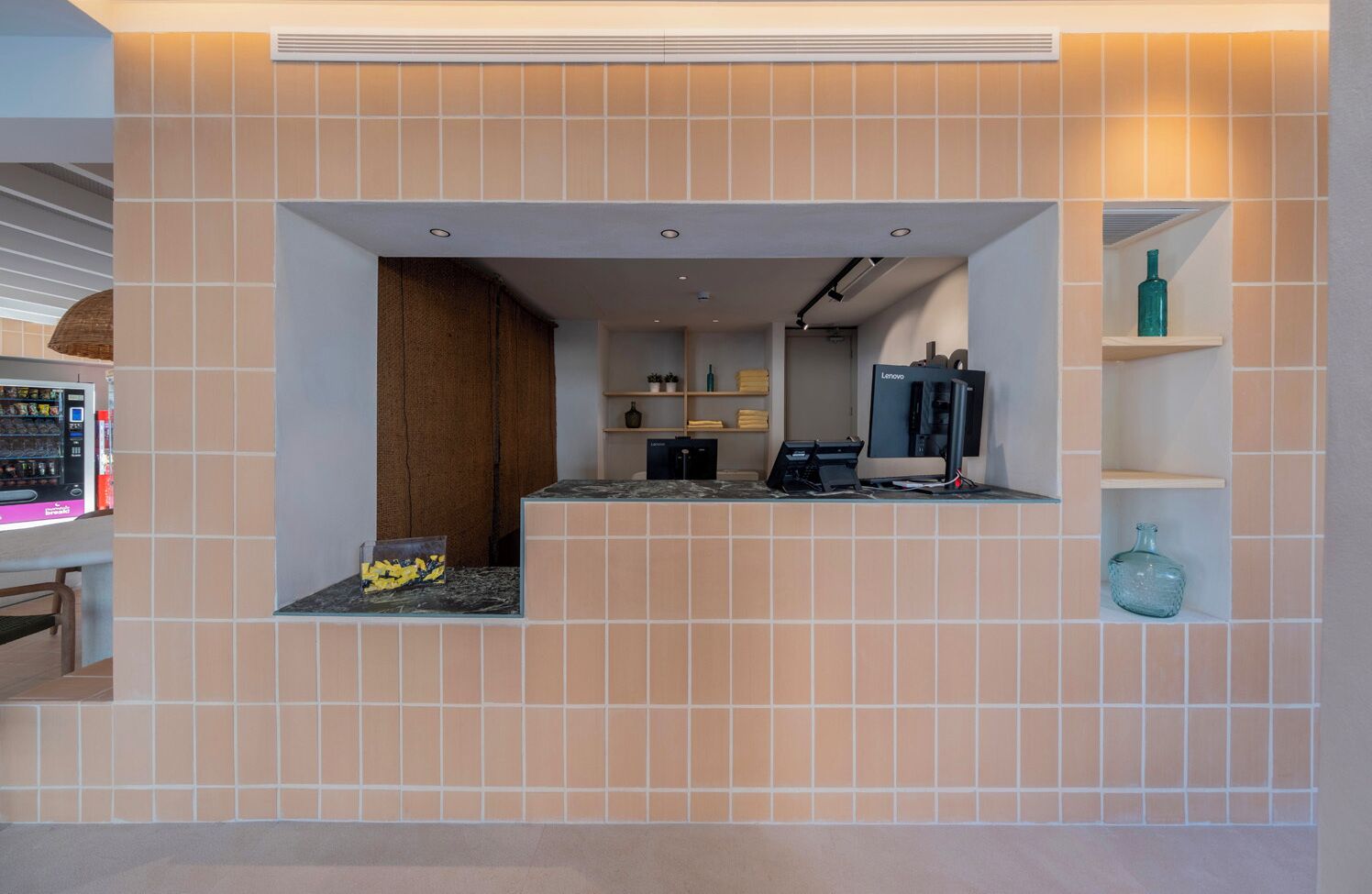 A modern reception area with a tiled wall, a counter with a computer, and a vending machine.
