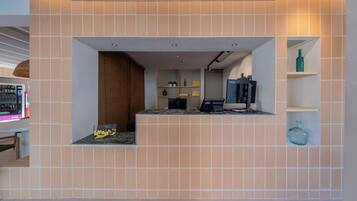 A modern reception area with a tiled wall, a counter with a computer, and a vending machine.