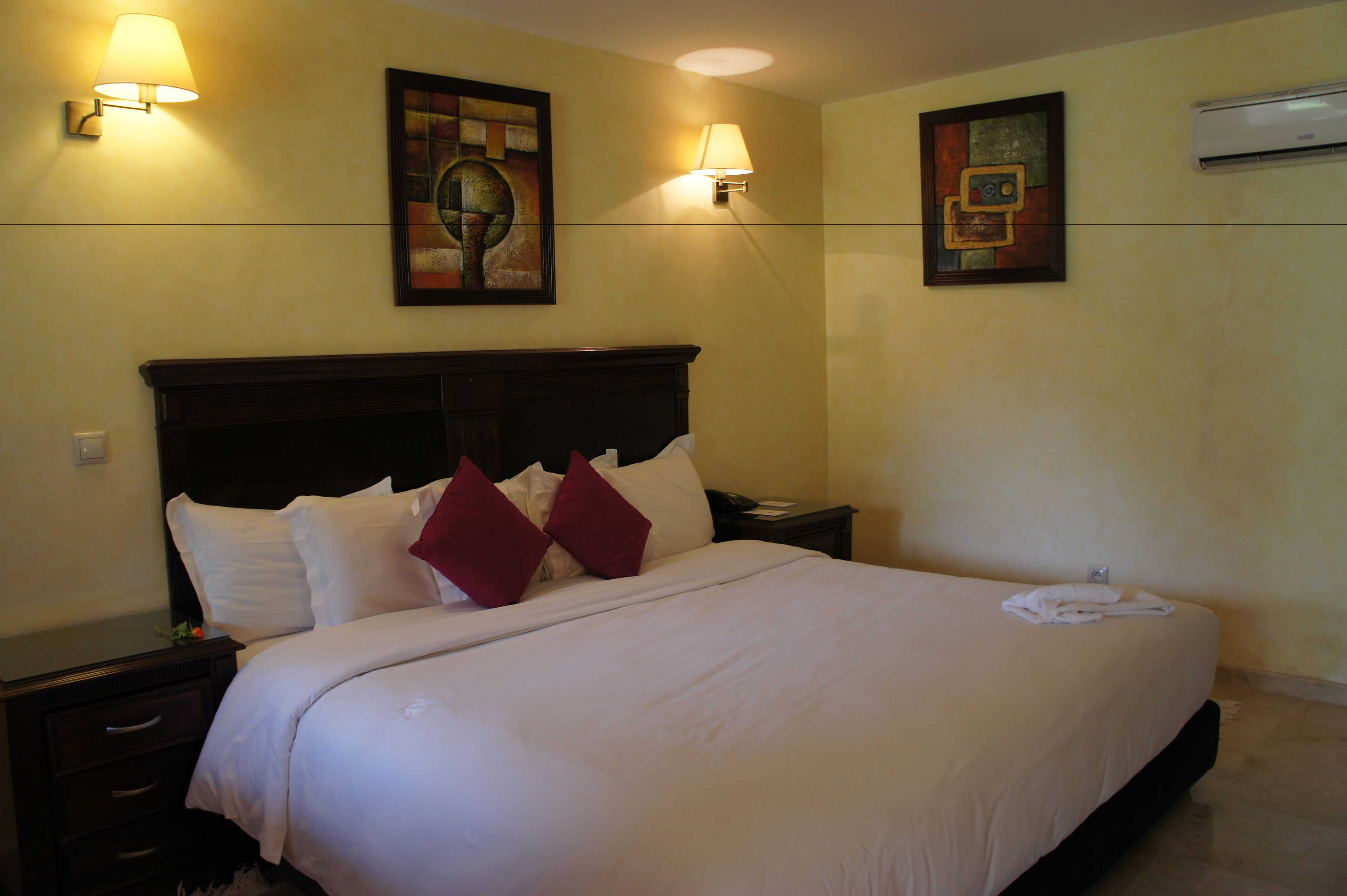 A hotel room with a large bed, two bedside lamps, and two framed artworks on the walls.