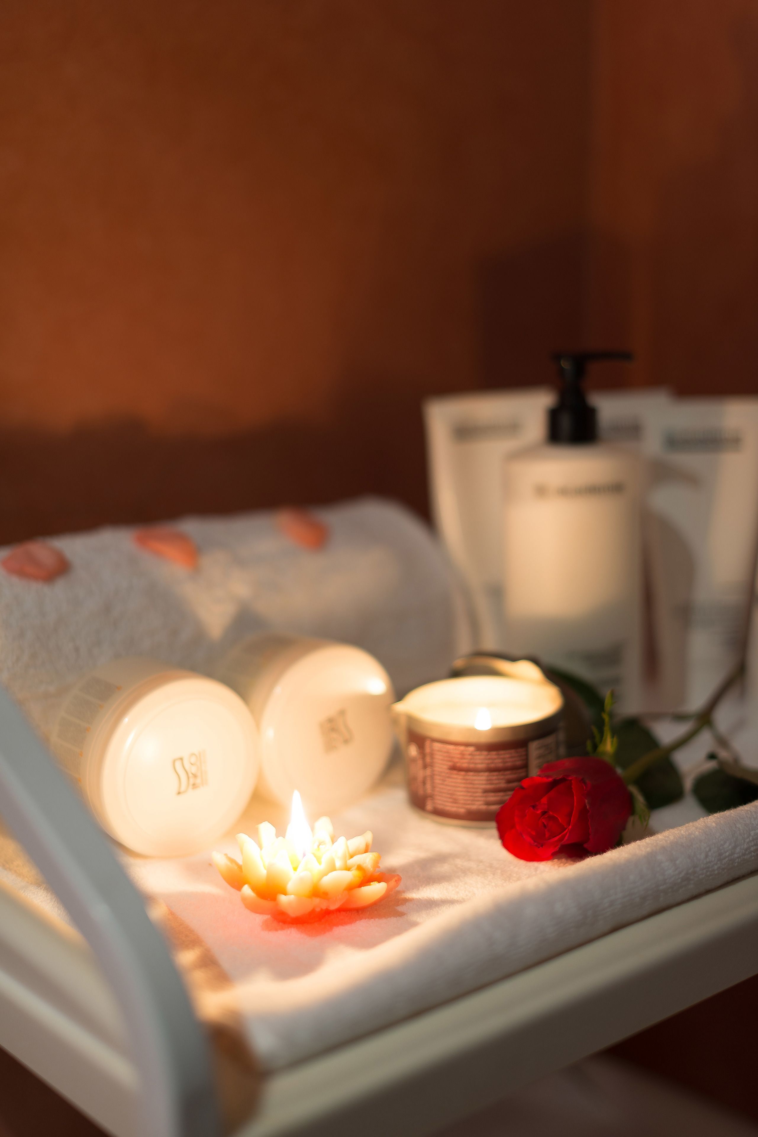 A spa setting with candles, a rose, and skincare products on a towel.