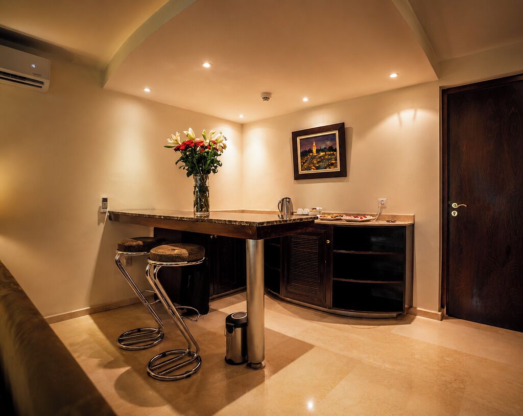 A kitchen with a bar stool, a vase with flowers, a framed picture on the wall, and a door.