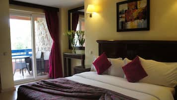A hotel room with a bed, a nightstand, a lamp, a painting, and a view of the outside.