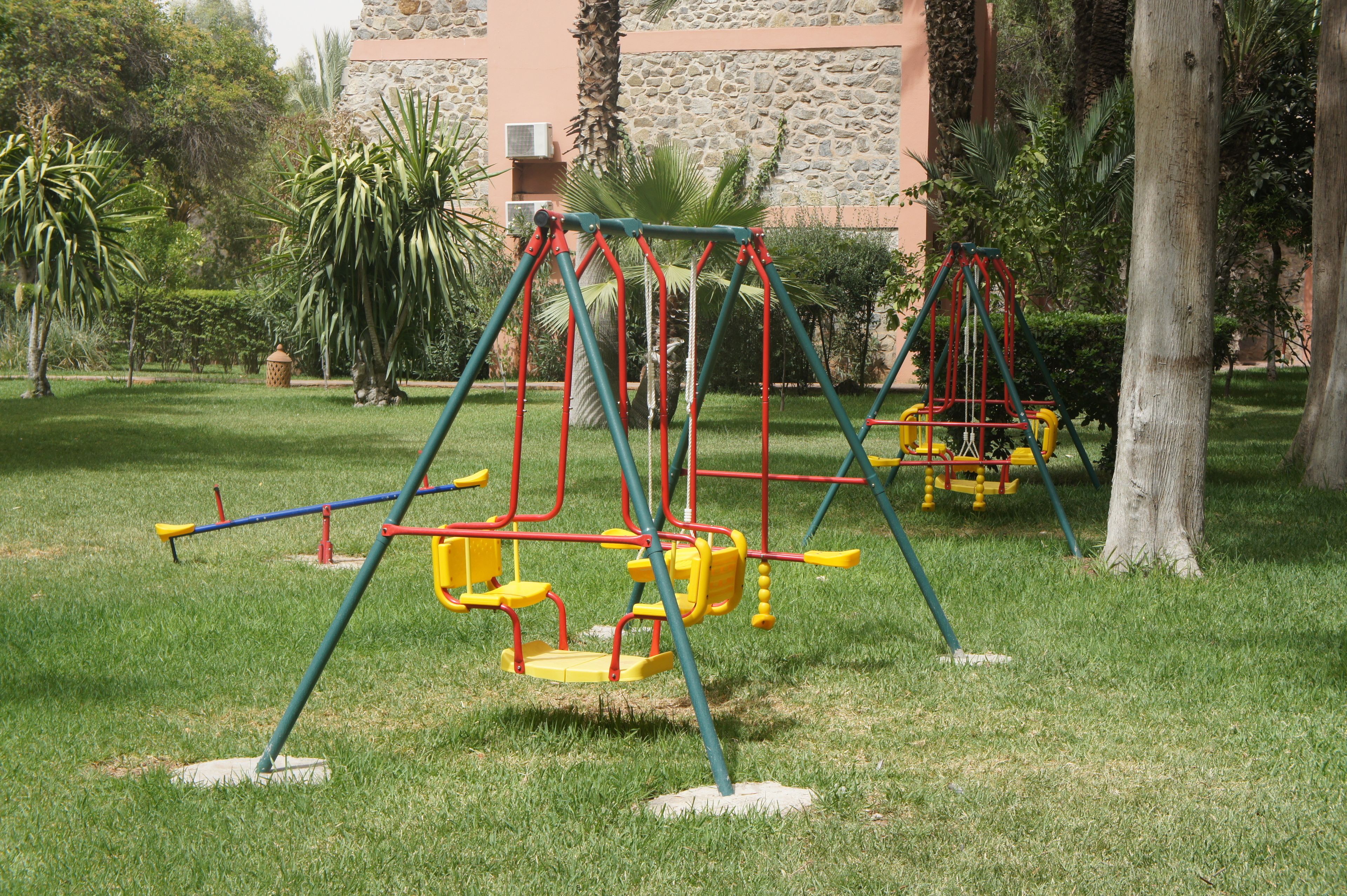 A playground with swings and a climbing structure in a park with grass and trees.