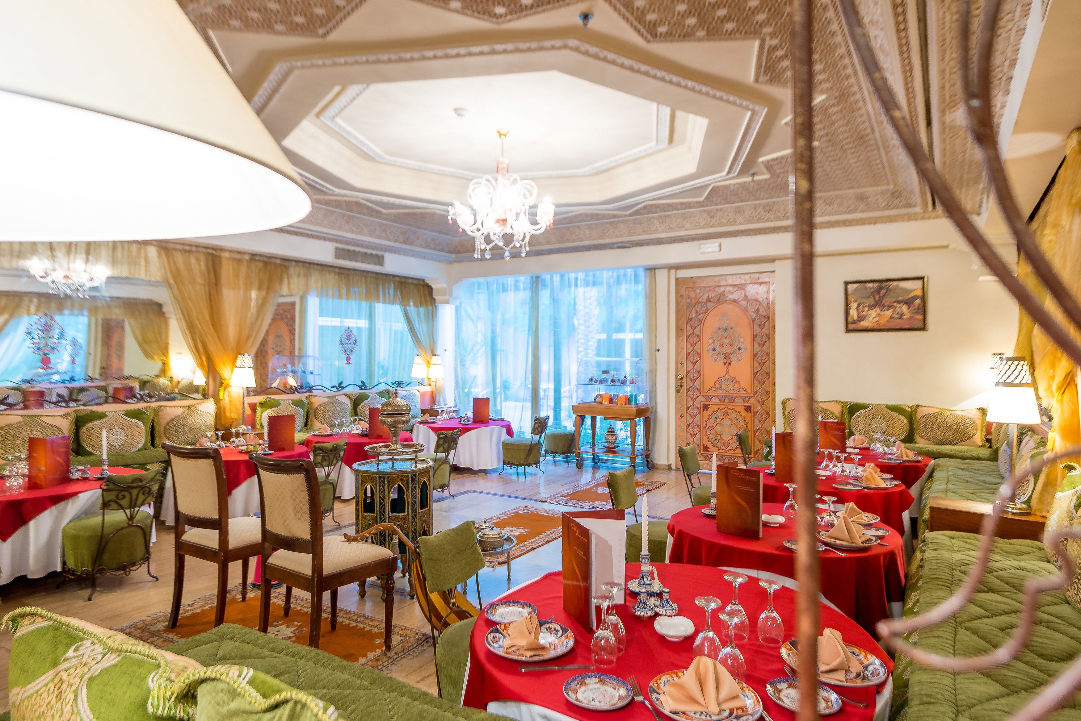 A luxurious dining area with multiple tables set for service, elegant chairs, and a chandelier.