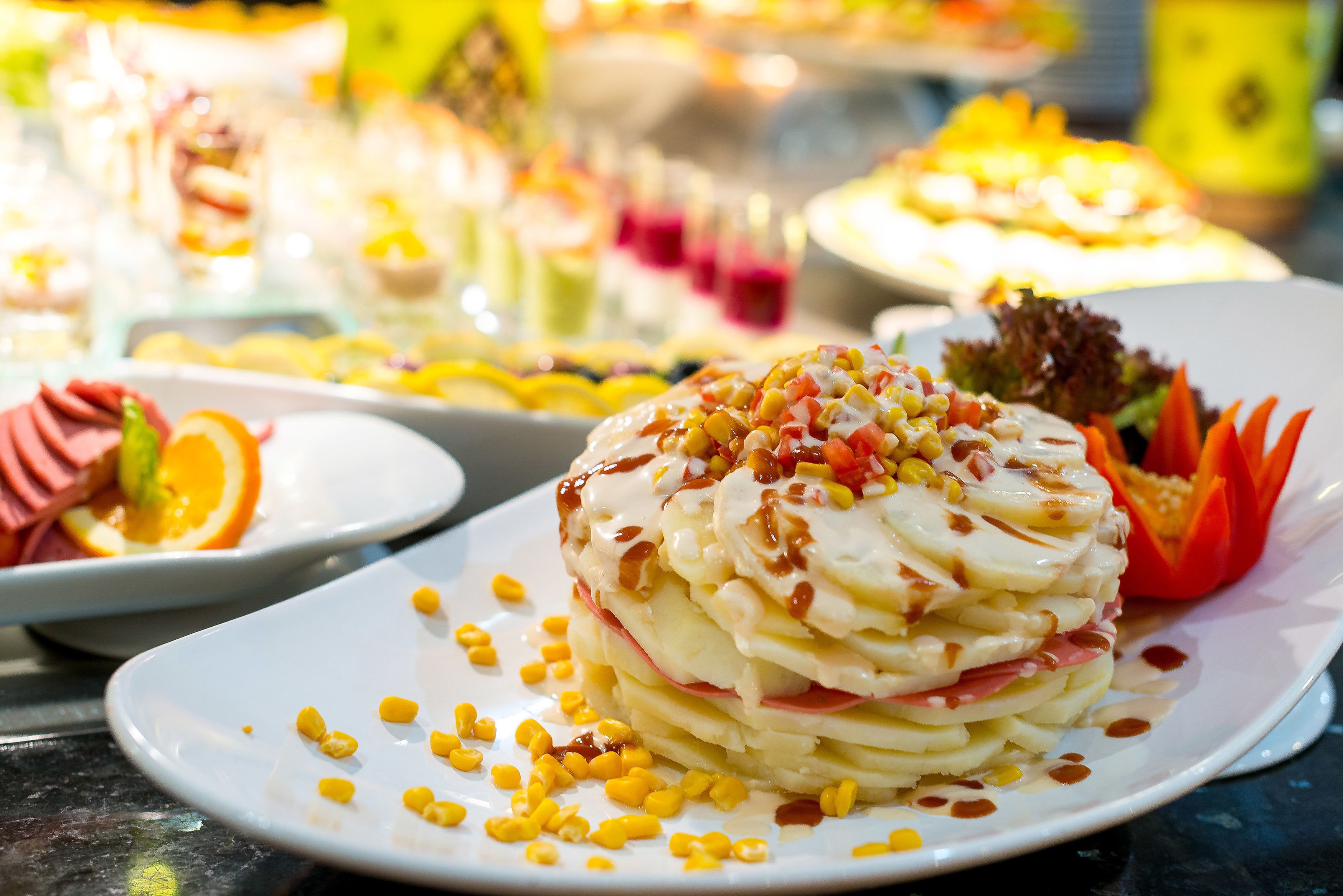 A variety of dishes on a buffet table, including a layered dessert with corn and a salad with orange slices.