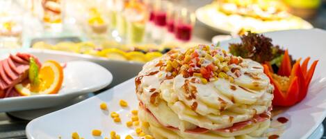 A variety of dishes on a buffet table, including a layered dessert with corn and a salad with orange slices.