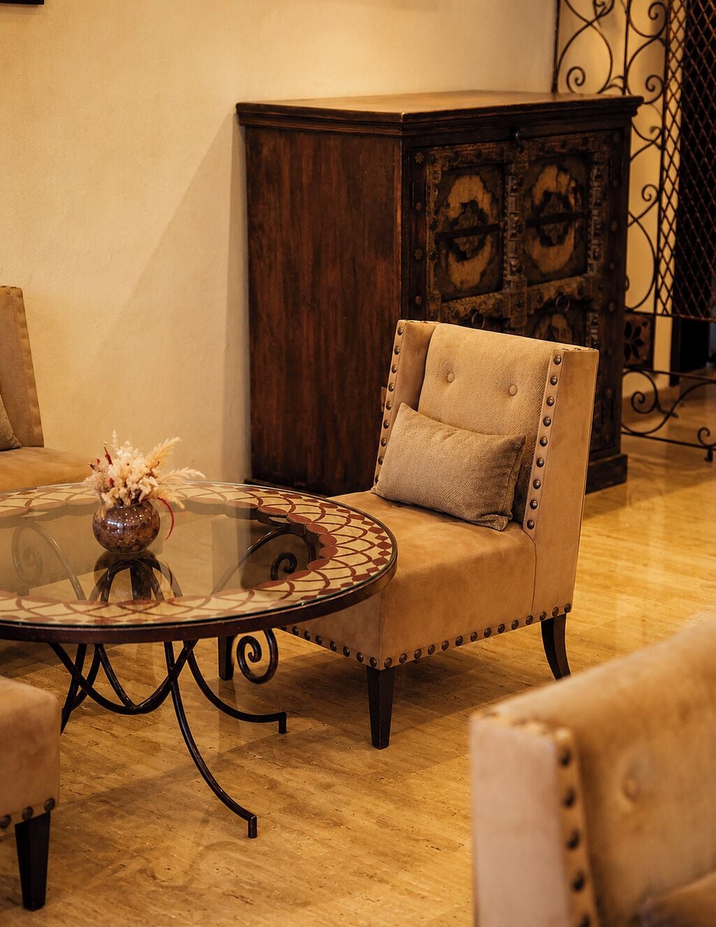 Una habitación con una mesa redonda de cristal, un sillón mullido, un armario de madera y un jarrón decorativo.