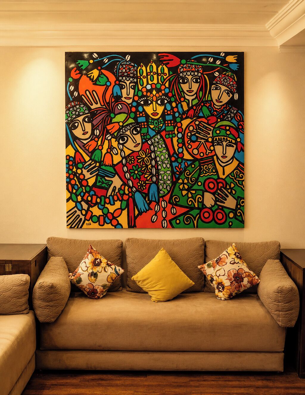A living room with a beige sofa, two patterned throw pillows, and a colorful abstract painting on the wall.