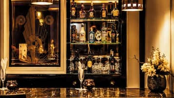 Una zona de bar con mostrador de mármol, dos lámparas colgantes, una variedad de botellas de licor, vasos y un espejo decorativo.