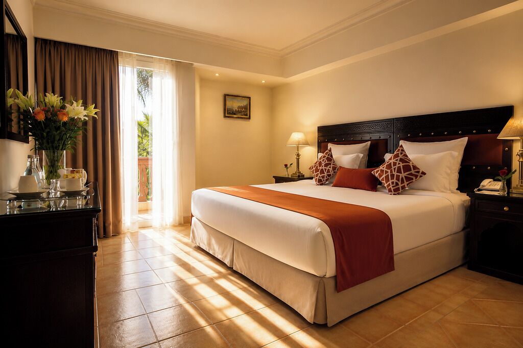A hotel room with a large bed, a desk with a vase of flowers, and a view of the outdoors.