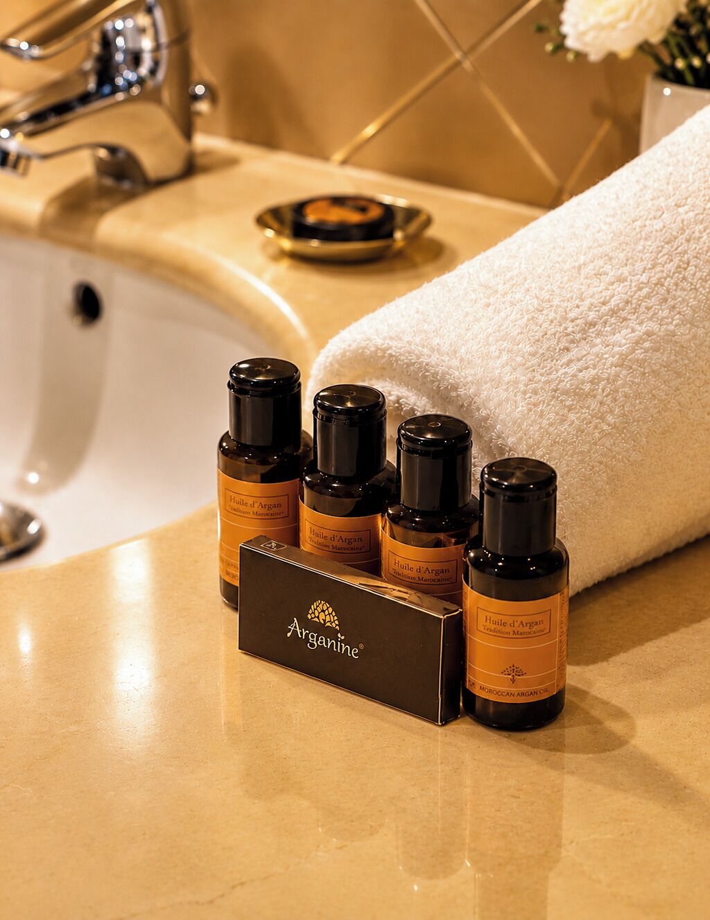 A bathroom with a sink, a towel, and a bottle of Argan oil.