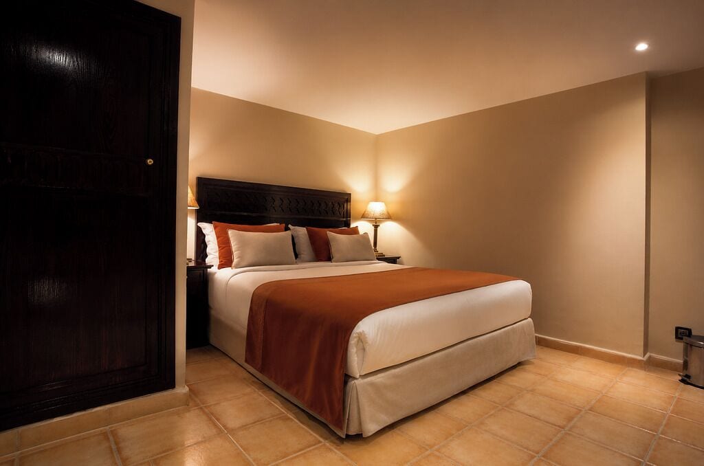 A hotel room with a large bed, a wooden headboard, two bedside lamps, and a dark door.