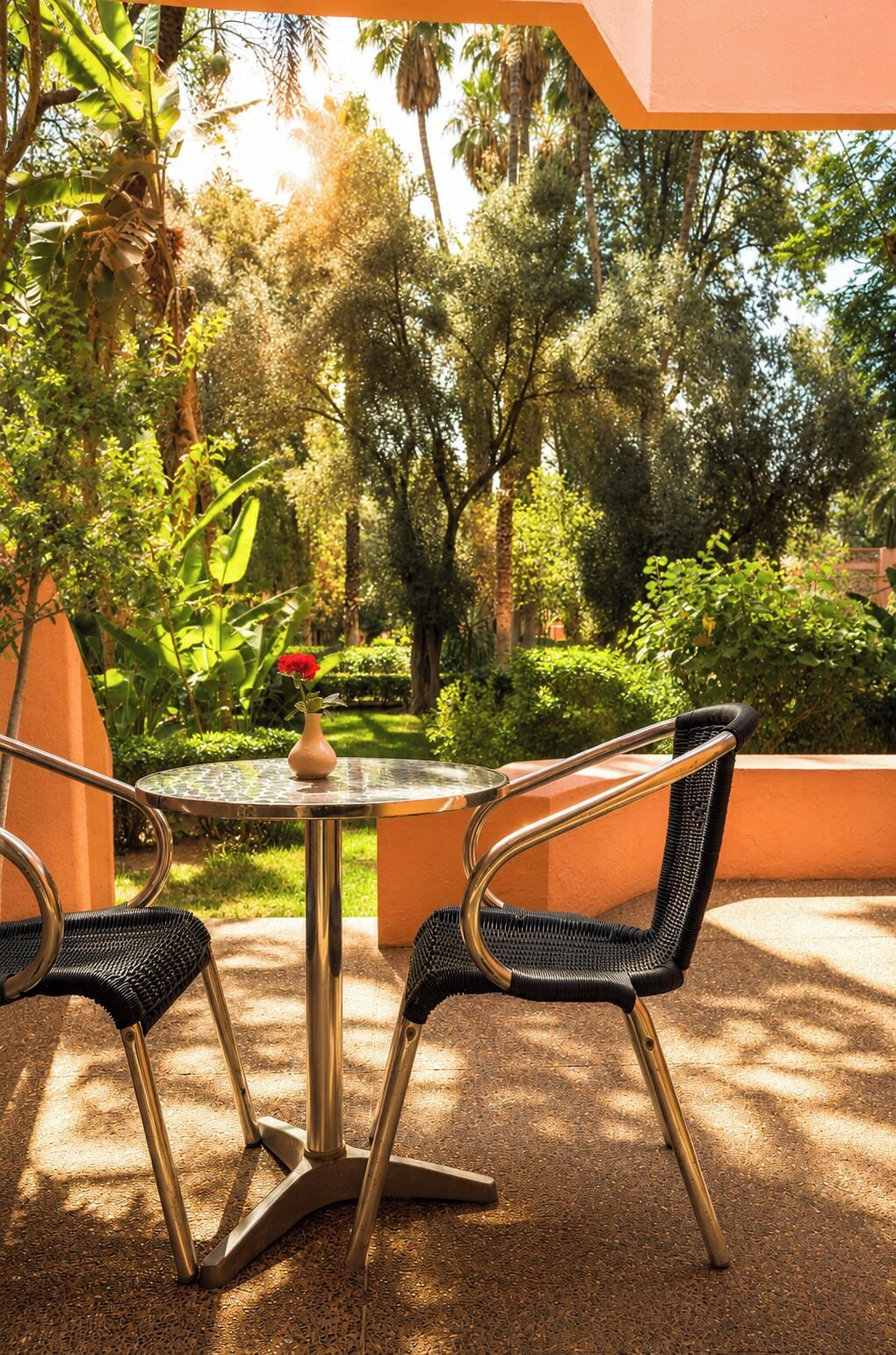 Un espace extérieur aménagé avec une table ronde et deux chaises, entouré d’une végétation luxuriante et de palmiers.