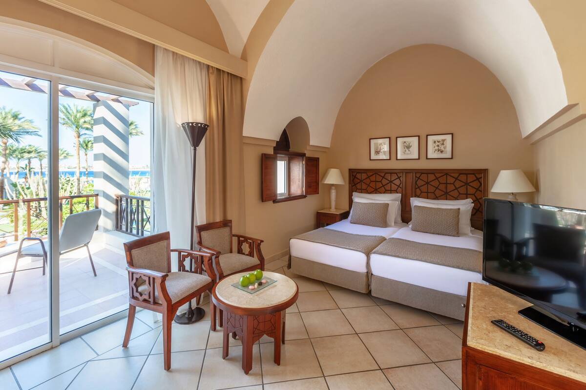 A hotel room with a bed, TV, and seating area with a view of palm trees.