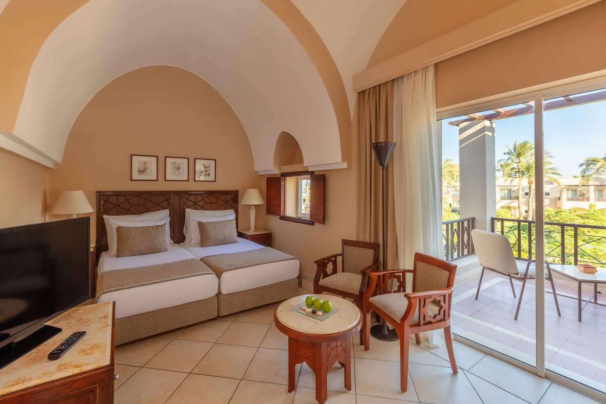 A hotel room with a bed, TV, and a balcony with a view of palm trees.