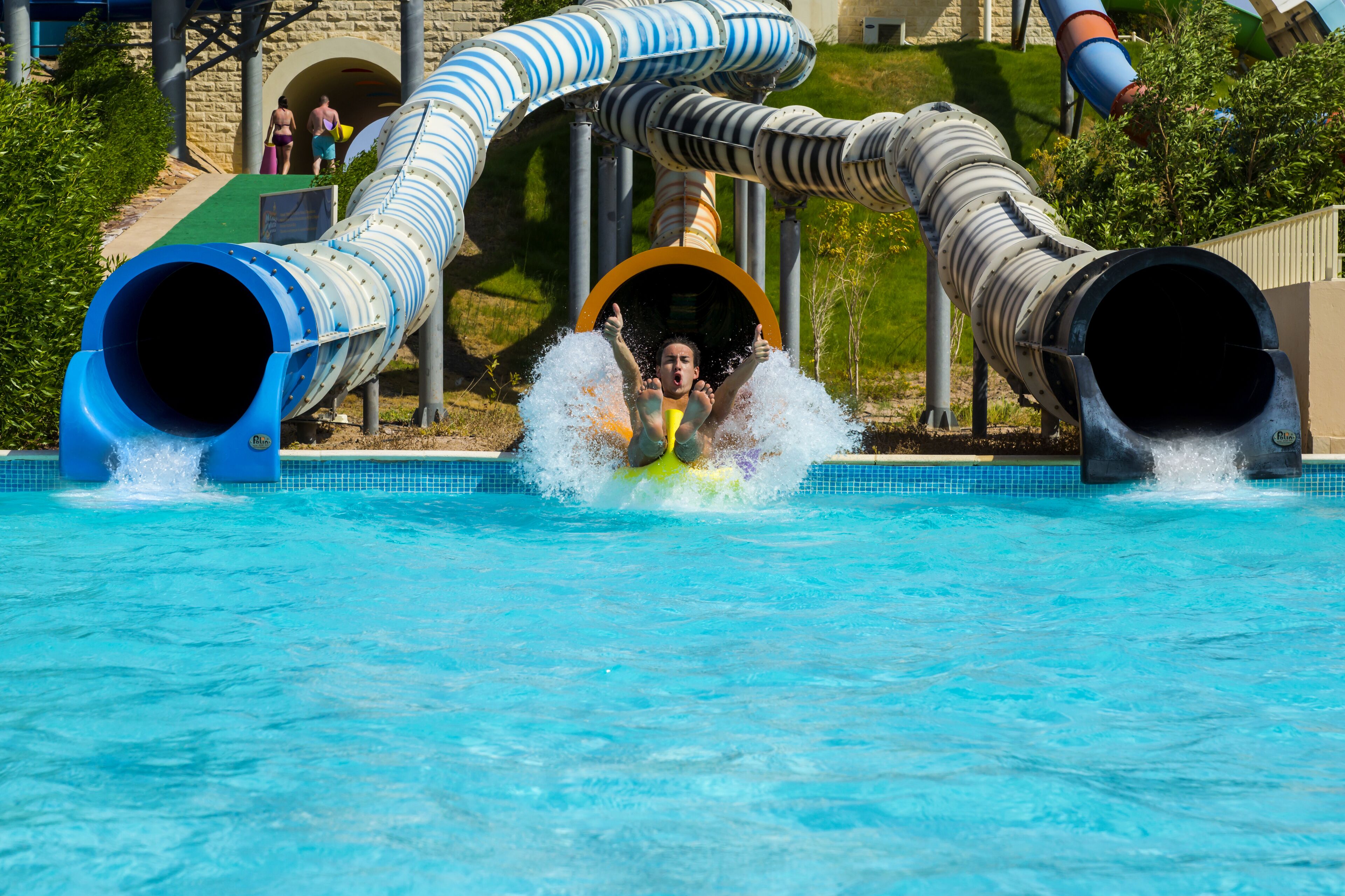Un toboggan aquatique se terminant par une zone où une personne peut atterrir, le tout entouré d’une piscine.