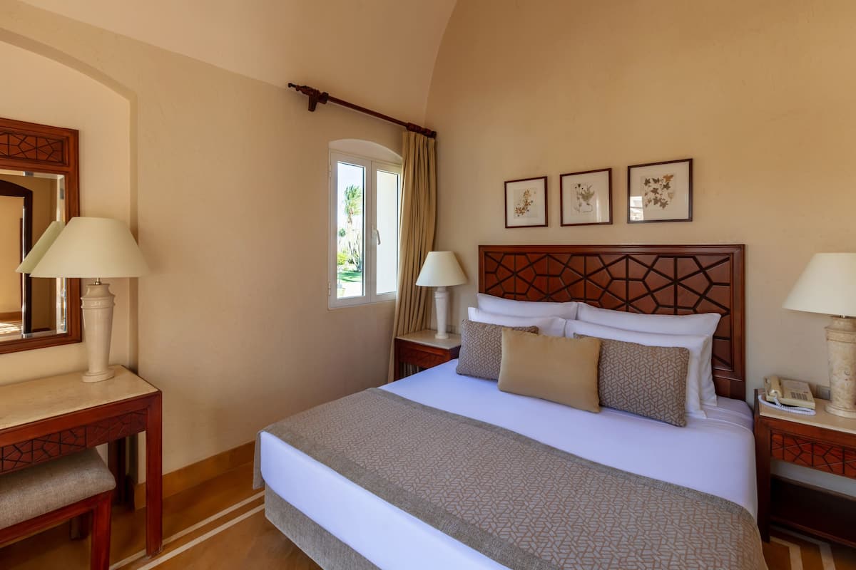 A hotel room with a large bed, two bedside tables with lamps, a wooden headboard, and a window with curtains.