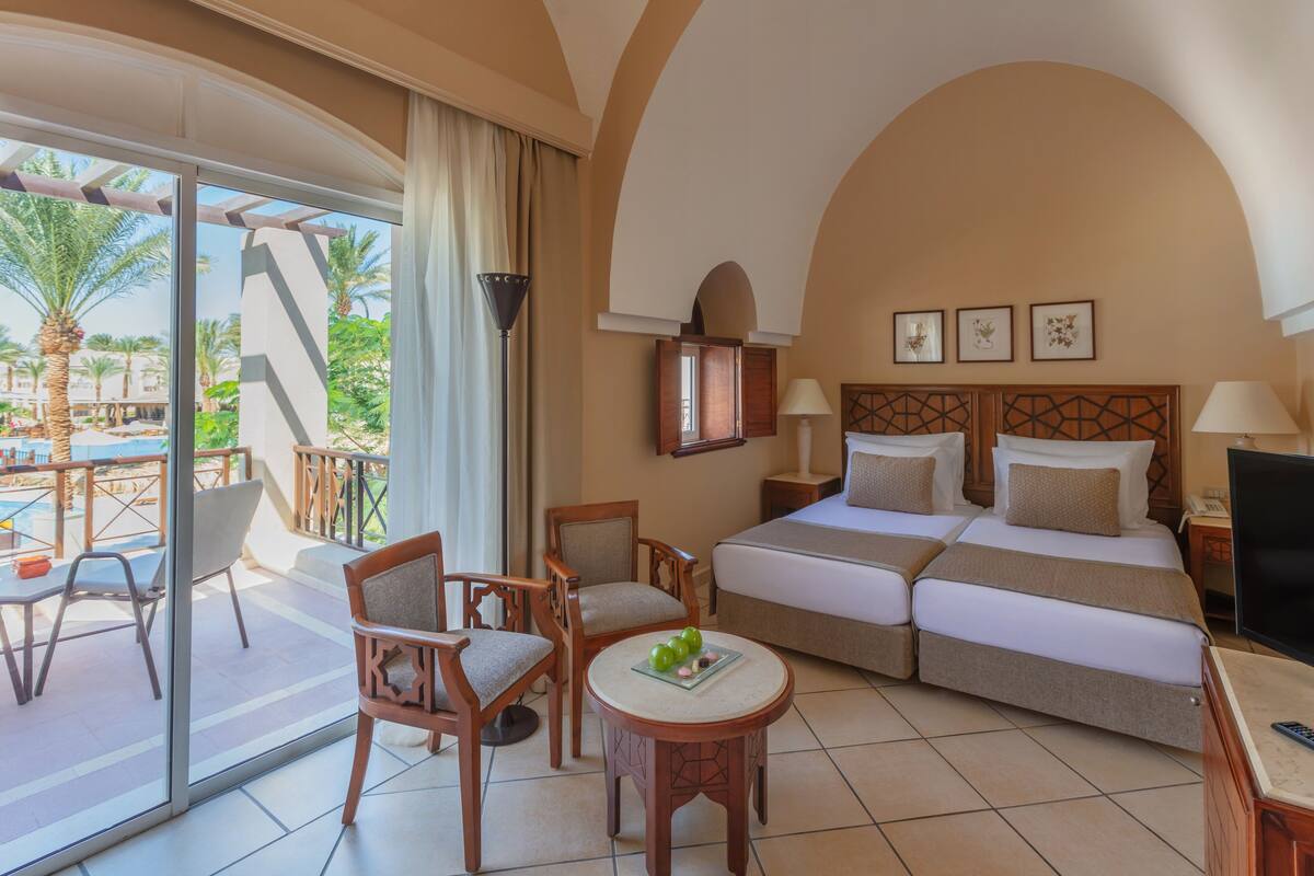 A hotel room with a balcony, two beds, a TV, and a dining table with chairs.