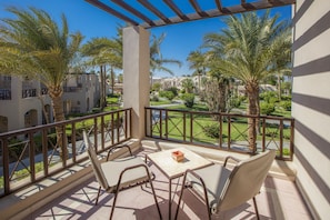 A balcony with a view of a golf course, palm trees, and a building with arches. - Iberotel Makadi Beach by JAZ - All inclusive (Makadi Bay)