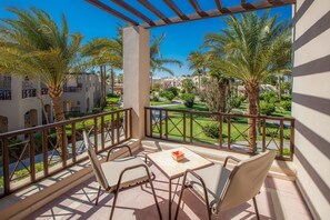 A balcony with a table and chairs, overlooking a landscaped area with palm trees and a golf course. - Iberotel Makadi Beach by JAZ - All inclusive (Makadi Bay)