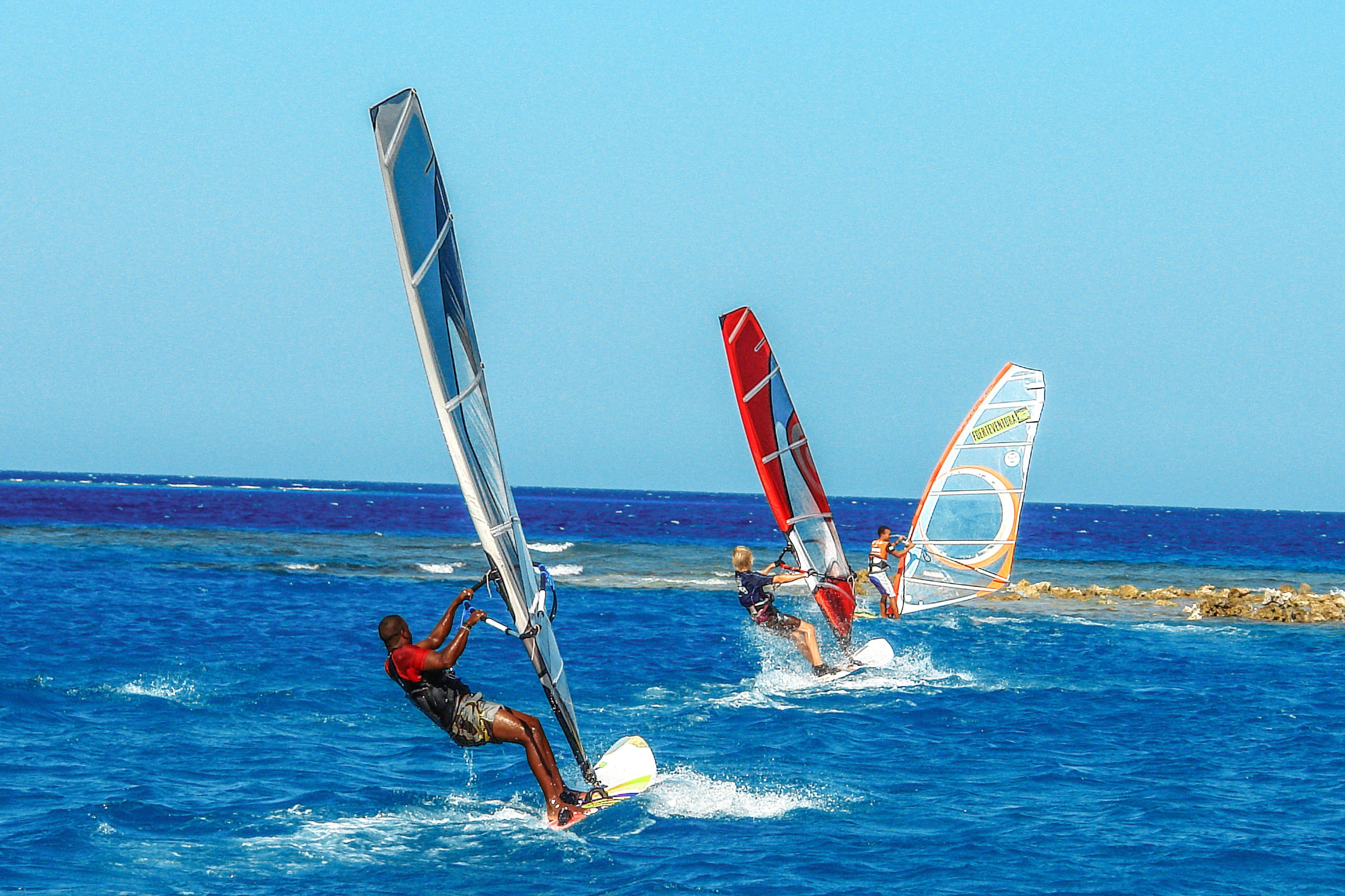 Three windsurfers on a clear blue sea.