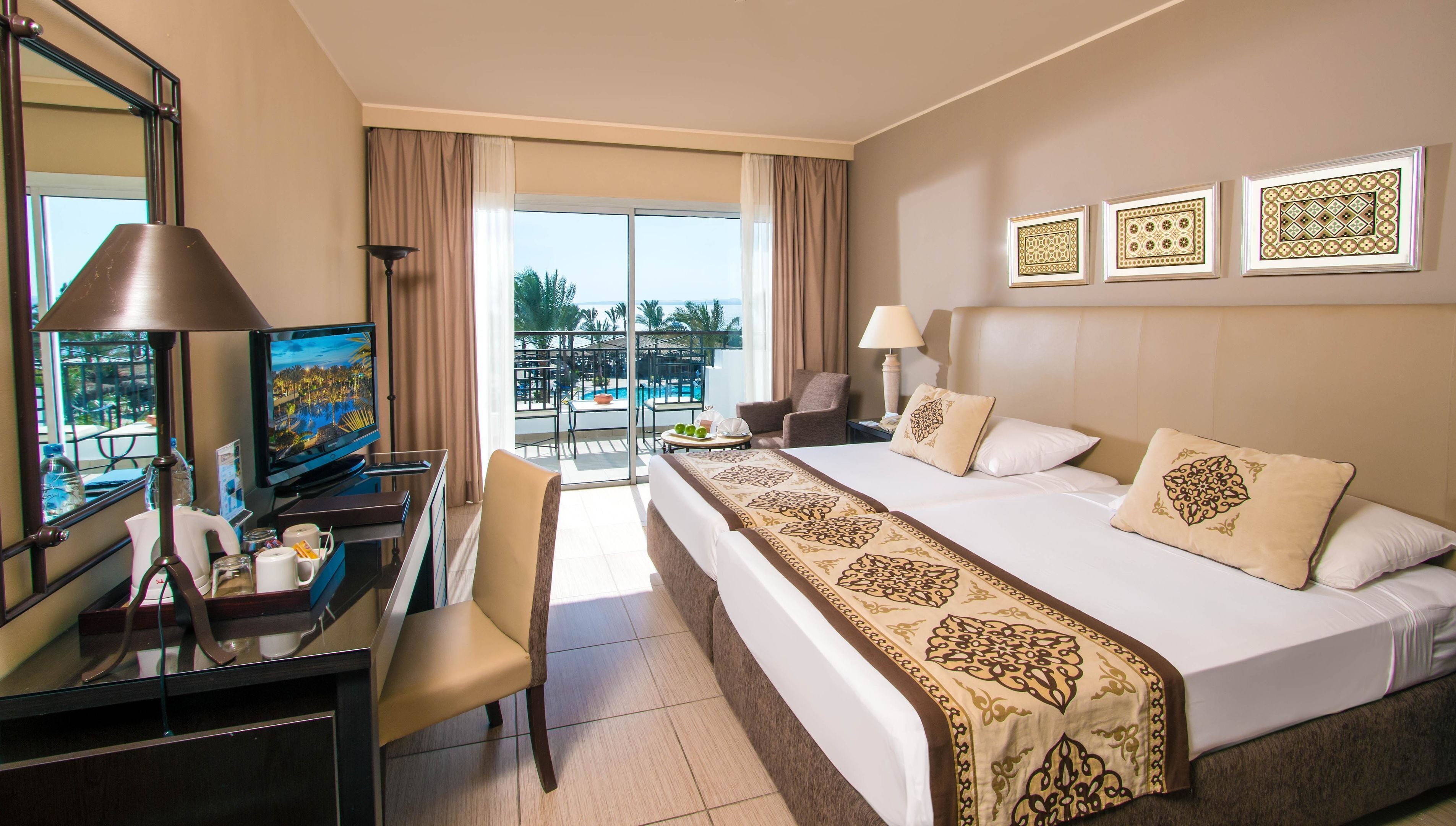A hotel room with a bed, desk, chair, and a balcony with a pool view.
