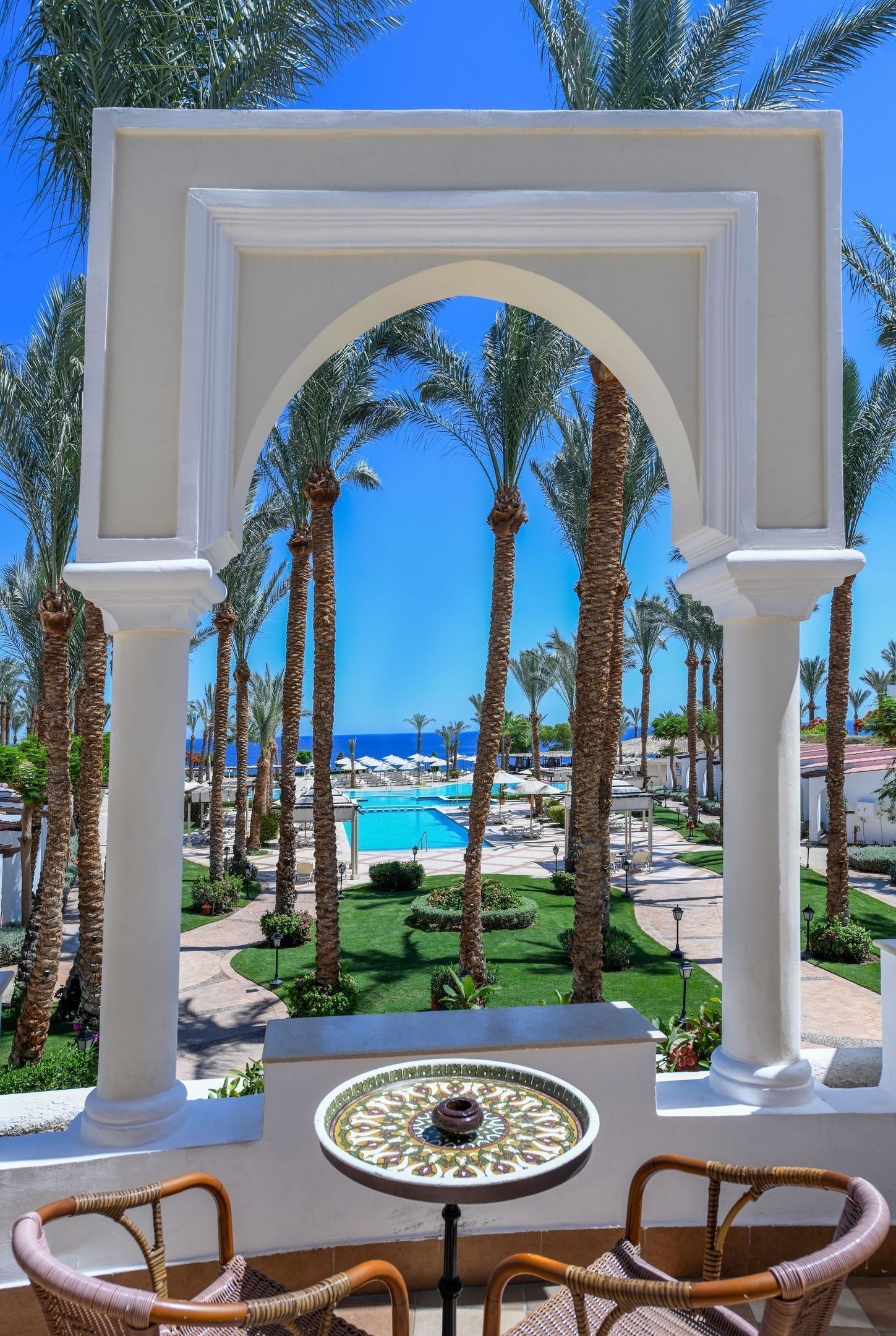 Una vista attraverso un arco bianco, con palme e una piscina sullo sfondo.