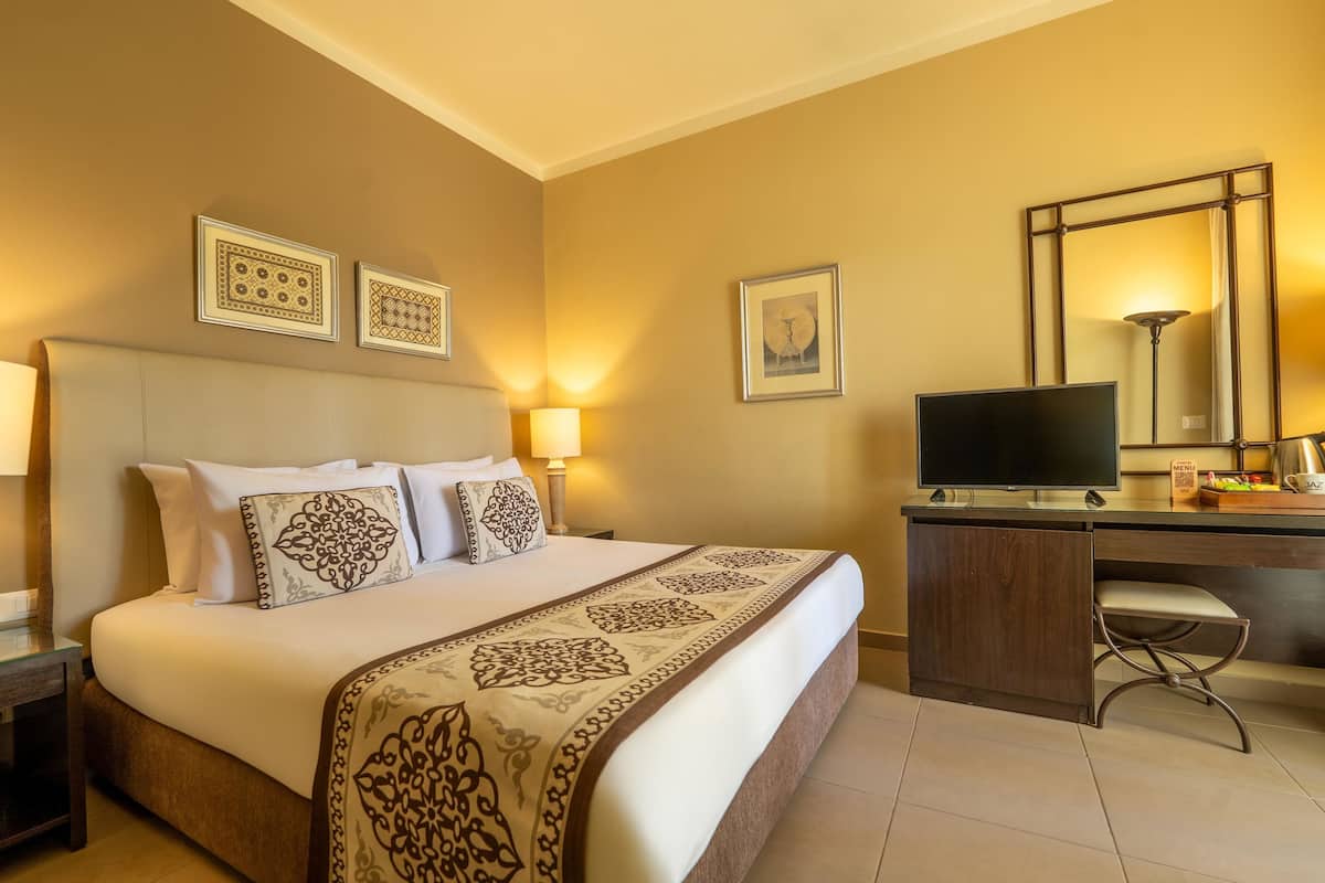 A hotel room with a bed, bedside table, desk, TV, and a large mirror.