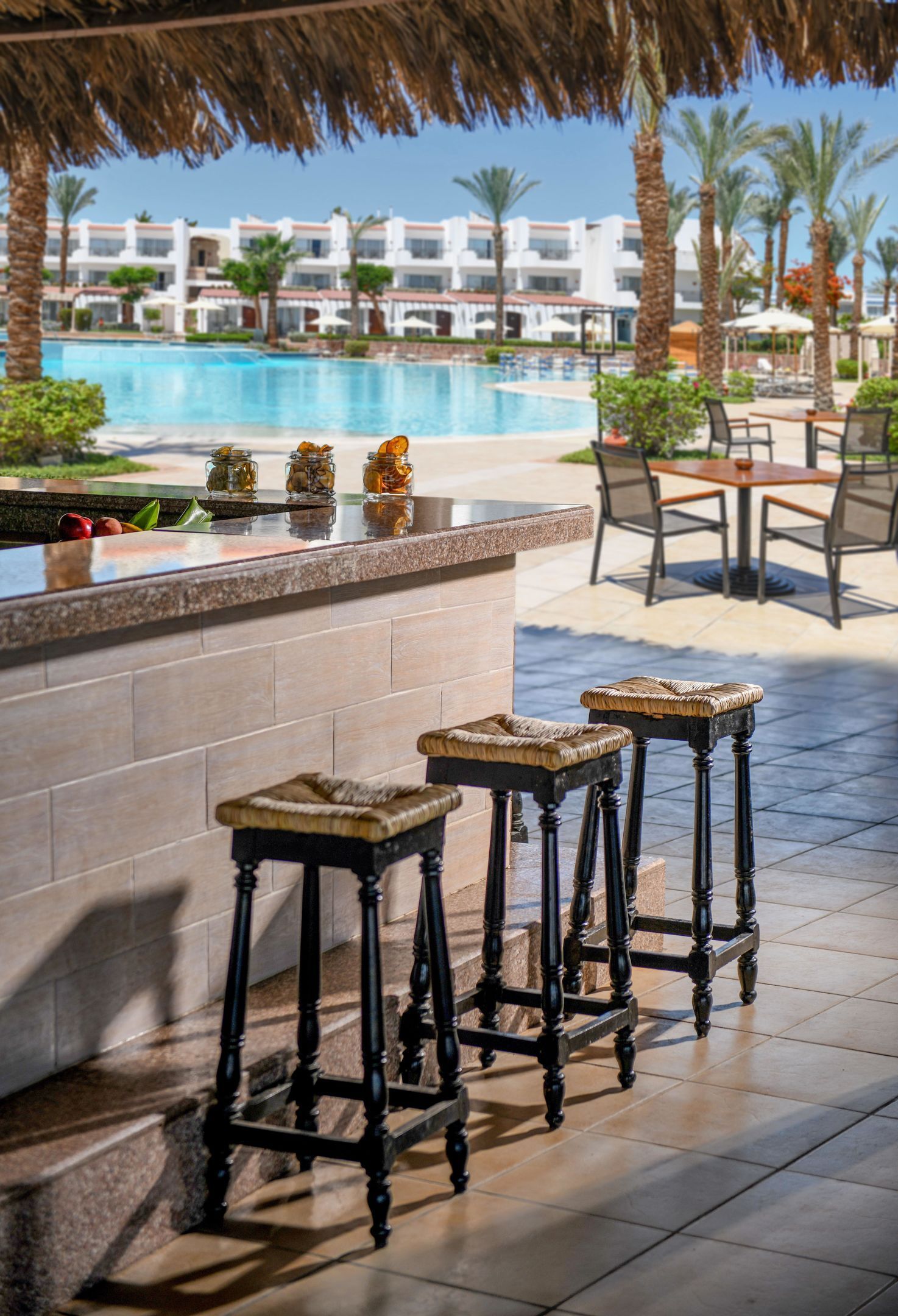 A poolside bar with stools, a pool, and a building in the background.