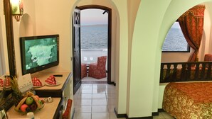 Une chambre d’hôtel équipée d’une télévision, d’un panier de fruits, d’un lit et d’un balcon avec vue sur la mer.