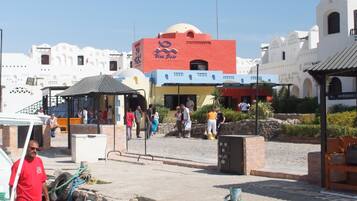 A coastal area with a blue boat docked at a pier, a building with a red and yellow facade, and a clear blue sky.