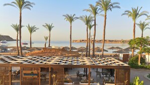 Un resort sulla spiaggia con posti a sedere all'aperto, palme e vista mare.