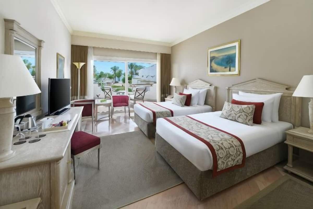Habitación de hotel con dos camas, un escritorio, televisión, una silla y vistas al exterior.