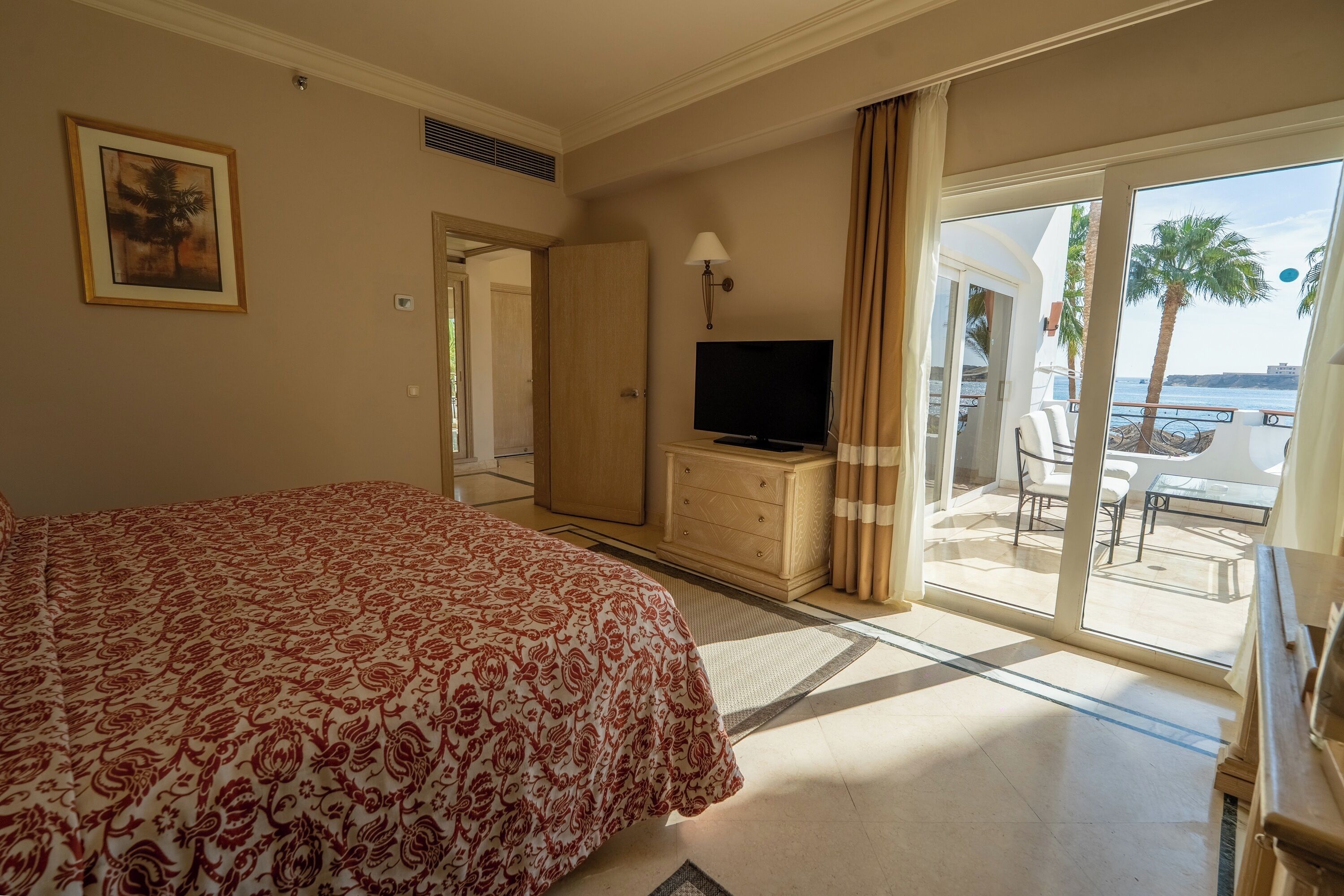 Habitación de hotel con una cama grande, televisión, escritorio y balcón con vista al mar.
