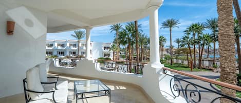 A balcony with a glass table and chairs, palm trees, and a view of a building complex.