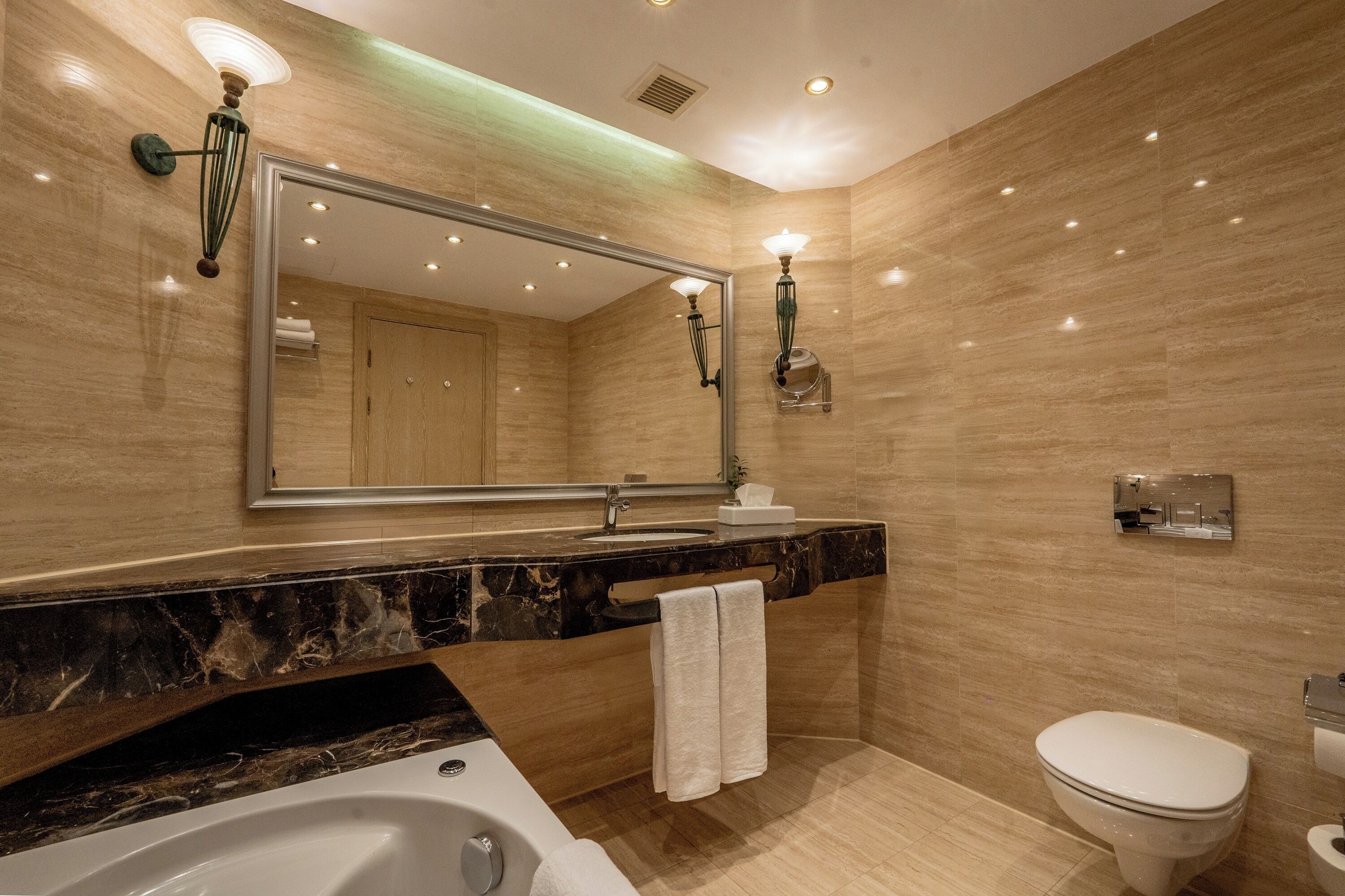 A modern bathroom with a marble countertop, a large mirror, a bathtub, and a toilet.