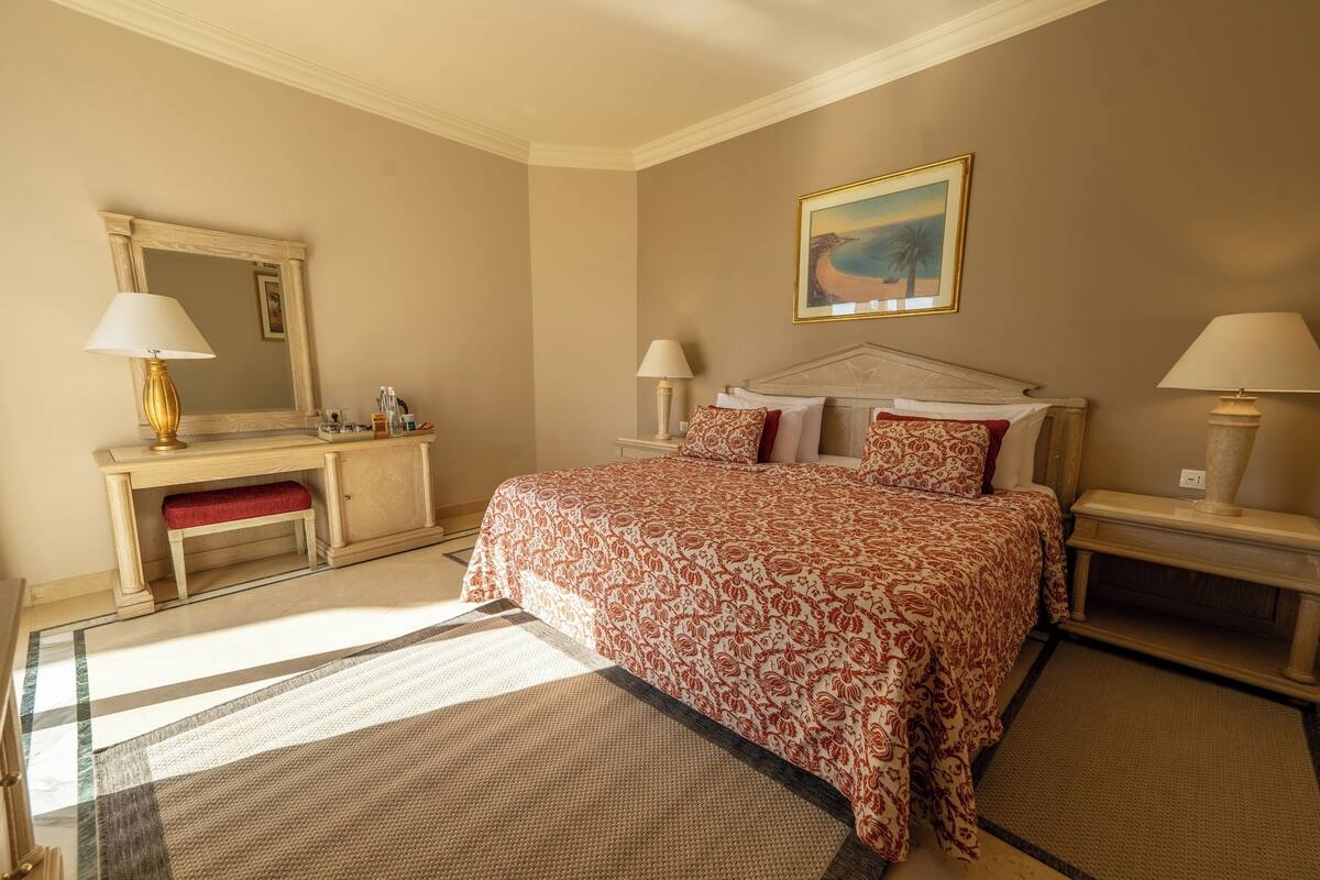 Een hotelkamer met een groot bed, een nachtkastje, een bureau met stoel, een spiegel en een schilderij aan de muur.